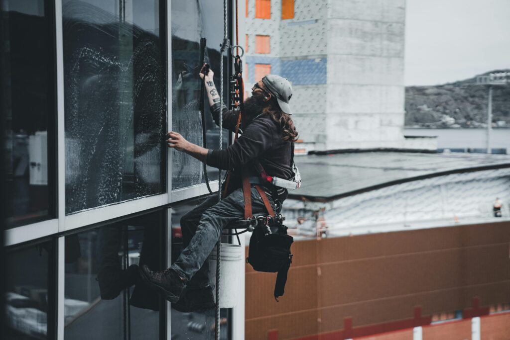 A man cleaning skyscraper windows with a harness, showcasing urban high-rise work.